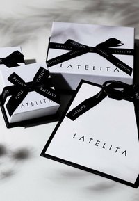 White gift boxes with black ribbons and "LATELITA" branding; varying sizes, rectangular shapes, smooth texture, contrasting color scheme.