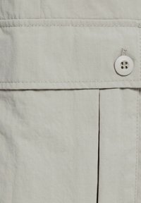 Světle šedá tkanina se strukturou, která obsahuje jemné mřížkové vzory, záhyb a detail knoflíku; šité švy jsou viditelné po celém povrchu.