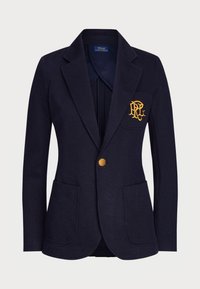 Blazer azul marino hecho de tela texturizada, con solapas de muesca, dos bolsillos delanteros y un parche de logo dorado en el pecho.