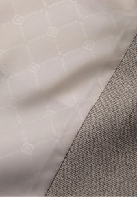Tissu en soie beige clair avec un motif géométrique "ombré" subtil à côté d'un tissu gris tissé texturé.