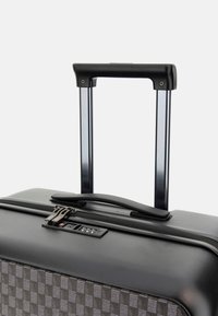Valise rigide noire avec un motif texturé gris, poignée rétractable, double zippée et serrure à combinaison.
