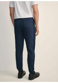 Granatowe spodnie dresowe z miękkiego materiału, z tylną kieszenią, elastycznymi mankietami i detalami na bocznych panelach. W zestawie z czarnymi sneakersami.