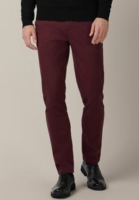 Burgundowe chinos o dopasowanym kroju, gładka bawełniana tkanina, płaski fason z przodu i tradycyjne kieszenie, w połączeniu z czarnymi skórzanymi butami.
