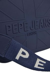 Bolso bandolera en azul marino con el logo grabado "Pepe Jeans London", superficie texturizada y una correa de tela con letras tejidas.
