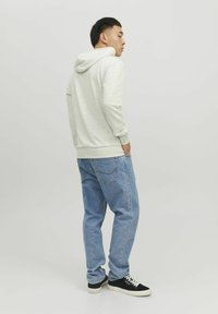 Lys grå hoodie med en frontlomme og snore, parret med afslappede blå denimjeans og sorte sneakers med hvide såler.