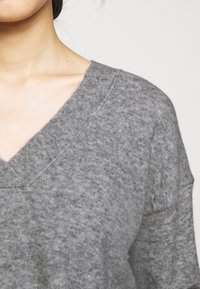 Maglione grigio lavorato a maglia con scollatura a V, caratterizzato da una consistenza morbida e una vestibilità ampia, che mette in mostra leggere variazioni nello spessore del filo.