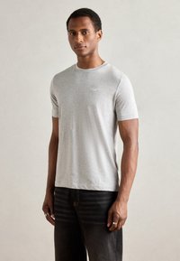 Tricou gri cu mânecă scurtă, fabricat dintr-un amestec de bumbac moale. Prezintă un decolteu tip echipaj și un branding subtil pe piept. Asortat cu blugi negri.