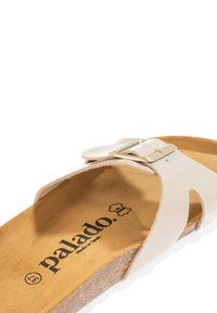 Sandalo slide beige chiaro in ecopelle con fibbia metallica. Presenta una soletta in sughero sagomata e suola in gomma bianca. Design semplice.