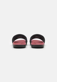 Chanclas negras con plantilla rosa. Diseño abierto y redondeado con suelas planas. Plantilla texturizada para mayor agarre. Estilo minimalista sin hardware visible.