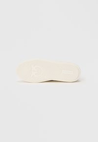 Suela de un zapato en goma blanco roto. Superficie texturizada con un patrón geométrico y un logotipo. Diseño plano con ligera curvatura en los bordes.