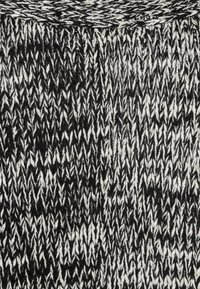 Pletená látka s černobílým zigzag vzorem, s texturovaným povrchem a různou tloušťkou nití pro vizuální zajímavost.