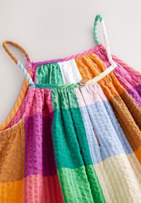 Robe sans manches multicolore avec bretelles réglables, présentant un tissu texturé en carrés de rose, vert, orange, bleu et blanc. Détail boutons en bois.