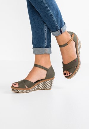 Olivekowe sandały na wedge z krzyżującymi się paskami, otwartym palcem i plecioną fakturą na obcasie. Brązowa podeszwa oraz pasek na kostkę z detalem klamry.