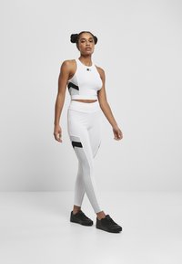 Crop top de sport blanc avec des accents noirs, associé à un legging blanc comportant des panneaux noirs et une texture lisse et extensible. Baskets noires.