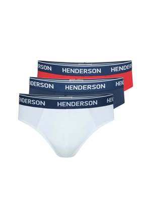 Hemdloser Mann mit kurzen lockigen Haaren, der weiße Slips mit einem dunkelblauen Bund trägt, der mit "HENDERSON" beschriftet ist, vor einfachem Hintergrund.