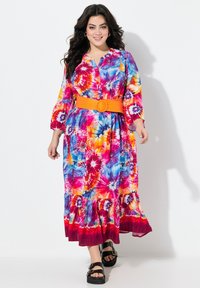 Barevné maxi šaty s tie-dye vzorem, které mají modré, růžové a oranžové vzory, dlouhé rukávy, zapínání na knoflíky vpředu a oranžový pásek s kulatou sponou.