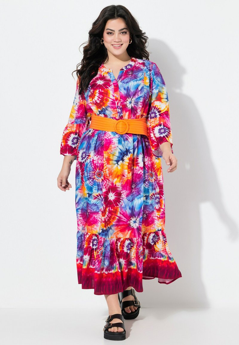 Kolorowa maksiodziana sukienka tie-dye z niebieskimi, różowymi i pomarańczowymi wzorami, długimi rękawami, zapięciem na guziki z przodu oraz pomarańczowym paskiem z okrągłą klamrą.