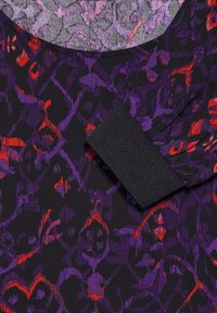 Zwarte stof met een paars en rood abstract bloemenpatroon, voorzien van een gestructureerde zwarte manchet. De gladde textuur complementeert het ontwerp.