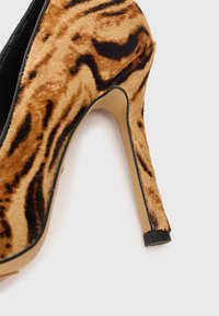 Chaussure à talon haut en imprimé léopard avec un matériau en fourrure texturé, doublure noire et un talon aiguille fin sur une semelle beige.