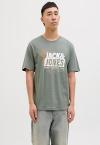 Alyvuogių spalvos medvilninis marškinėliai trumpomis rankovėmis, su dideliu baltu ir oranžiniu "JACK & JONES" grafiniu ir žemėlapio dizainu priekyje.