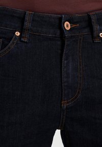 Mörkblå denimjeans med kontrasterande orange sömmar, knappgylf och framfickor. Mjuk textur med en slim fit-design.