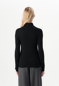 Pull en maille côtelée noir avec un col haut et des manches longues, ajusté au niveau du torse et s'évasant légèrement à l'ourlet.