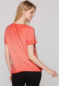 Camiseta de manga corta en un degradado de coral claro a oscuro, hecha de una tela suave y texturada. Presenta un cuello redondo y un ajuste relajado.