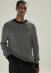 Pulover cu model alb și negru, cu guler rotund, manșete și tiv din material elastic. Prezintă un design geometric pe întreaga țesătură.