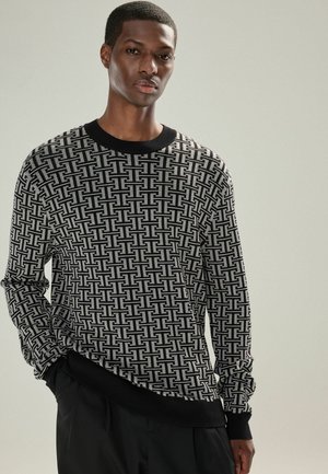 Pulover cu model alb și negru, cu guler rotund, manșete și tiv din material elastic. Prezintă un design geometric pe întreaga țesătură.