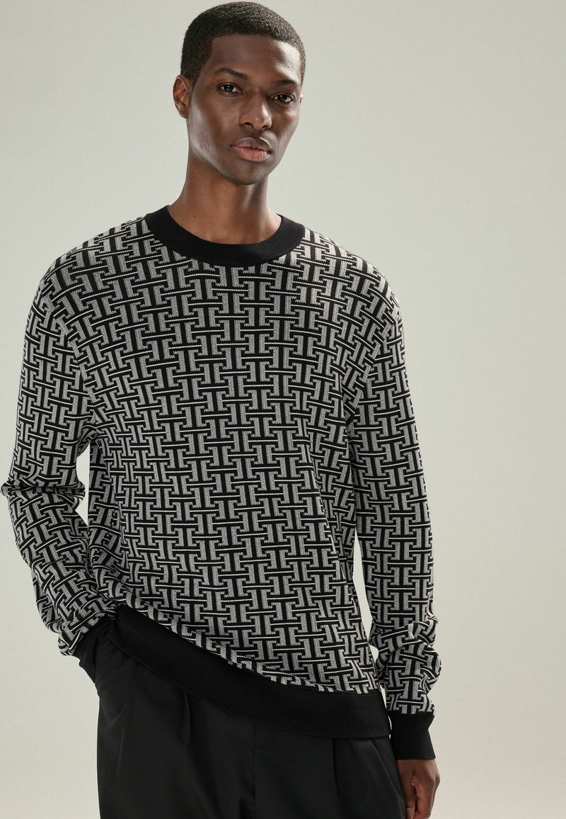 Pulover cu model alb și negru, cu guler rotund, manșete și tiv din material elastic. Prezintă un design geometric pe întreaga țesătură.