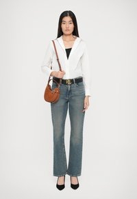 Balta pogāmā krekls, melna josta ar logo, gaiši zili platiem džinsi un brūna somiņa. Modelis valkā melnas papēžu kurpes.