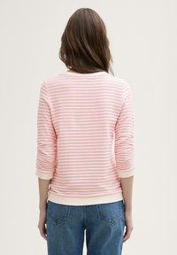 Pulover roz cu dungi, cu mâneci trei sferturi și mansete cu nervuri, având un model texturat și o croială lejeră, asortat cu blugi albaștri.