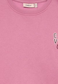 Sweatshirt rosa feito de tecido macio com gola redonda canelada. Apresenta um pequeno design impresso na frente e uma etiqueta indicando o tamanho 9-10 anos.