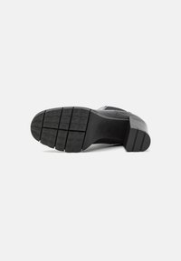 Suela de zapato negra con un diseño de goma texturizada, que presenta ranuras horizontales y un tacón bloque para estabilidad.