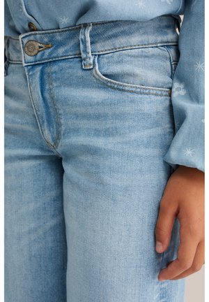 Nahaufnahme einer Person, die hellblaue Denim-Jeans und ein blaues Hemd mit weißen Schneeflockenmuster trägt, wobei die vordere Tasche und die Hand zu sehen sind.