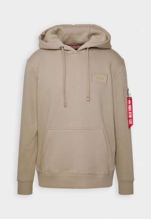 Beige Kapuzenpullover mit einer Fronttasche, einer Kapuze mit Kordelzug und einer Seitentasche mit einem roten Etikett. Weicher Stoff, gerippte Bündchen und Saum.