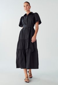 Juodas sluoksniuotas maksi suknelė su trumpomis pūstomis rankovėmis, mygtukų priekis, diržo juosmuo ir lygaus medvilnės audinio. Derinama su juodais sandalais ant juostos.