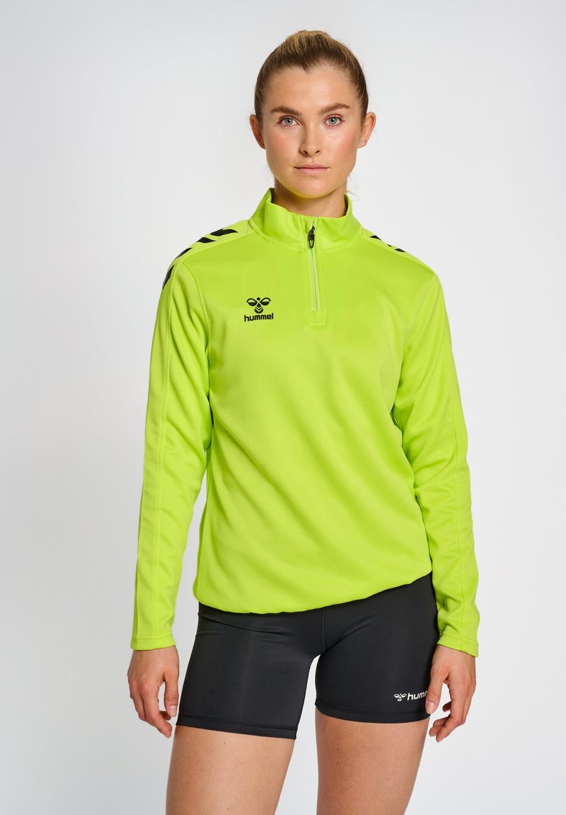 Heldergroen lange mouwen pullover met een halve ritssluiting en zwart logo, gecombineerd met zwarte sportshorts met logo-accenten.