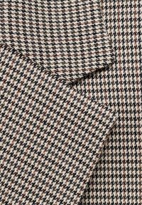 Tessuto di lana con un motivo houndstooth nei colori nero, bianco e rosso. La trama è densa con una superficie leggermente pelosa.