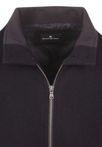 Zwarte zip-up jack met een geribbelde kraag, voorzien van een zilveren rits en een gladde voering aan de binnenkant. Merklabel is zichtbaar binnen in de kraag.