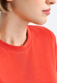 Korte mouwen crewneck t-shirt in levendig rood, gemaakt van een soepele stof met stikseldetails rond de halslijn en schouders.