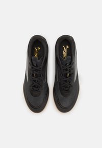 Zapatillas deportivas negras con un upper texturizado, que presenta un diseño estriado y cordones negros. Con detalles en dorado y una suela de goma.