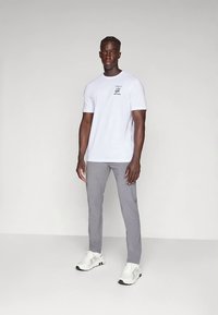 Hvit bomulls-T-skjorte med korte ermer og trykt aksent, kombinert med lysegrå bukser og hvite joggesko med svarte detaljer.