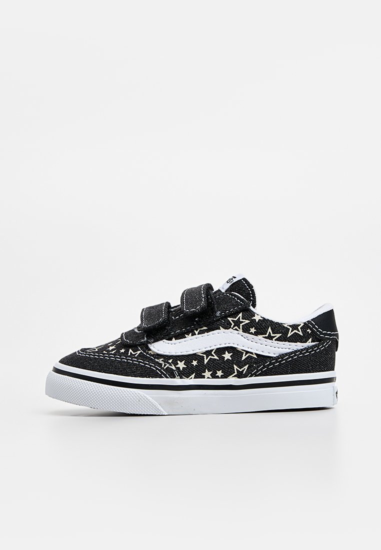 Zapato de lona negro con patrón de estrellas blancas y detalles en blanco, con correas de Velcro y suela de goma. Diseño bajo con punta redonda.