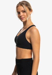 Top deportivo negro de corte corto con tirantes anchos, textura suave y diseño ajustado. Pantalones negros de cintura alta con bolsillos con cremallera.