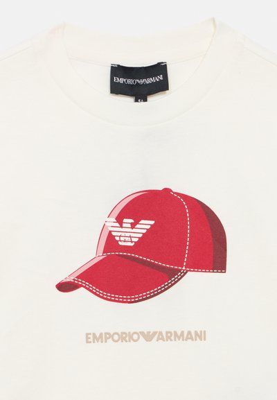 Λευκό T-shirt με κόκκινο γραφικό μιας καπέλου. Το καπέλο έχει λευκές ραφές και ένα λογότυπο. Το όνομα της μάρκας "EMPORIO ARMANI" είναι τυπωμένο από κάτω σε ανοιχτό χρώμα.