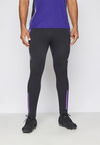 Leggings atletici neri con strisce laterali viola e un logo. Progettati per le performance, con una forma aderente e materiale elasticizzato.