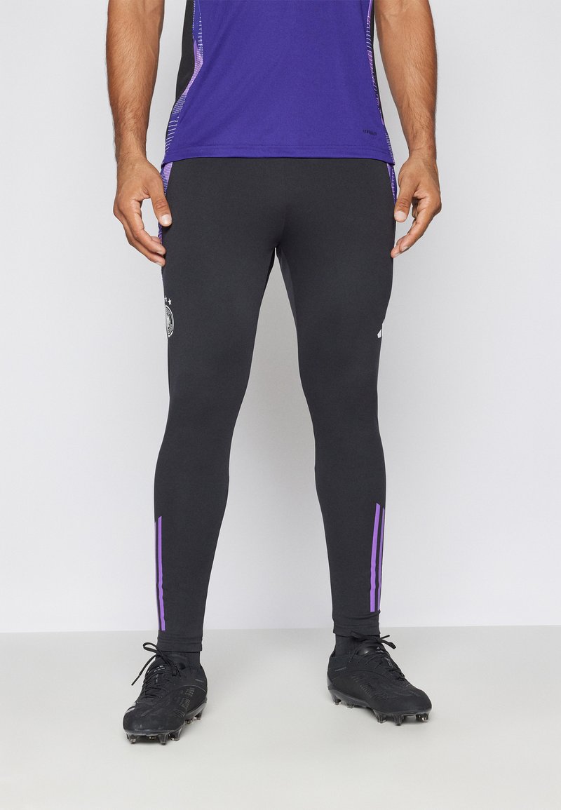 Leggings atletici neri con strisce laterali viola e un logo. Progettati per le performance, con una forma aderente e materiale elasticizzato.