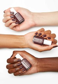 Trois mains présentent des bouteilles de vernis à ongles Essie dans des teintes de mauve profond. Les ongles sont soigneusement manucurés, avec un bouchon blanc sur les bouteilles en verre.