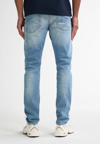 Jeans in denim azzurro chiaro con una vestibilità slim, caratterizzati da due tasche posteriori e un leggero scolorimento. Abbinati a sneakers di colore chiaro.
